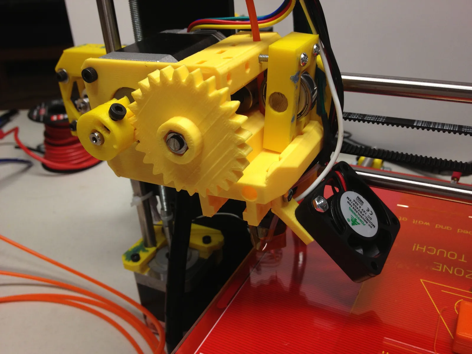 Extrusor de una Prusa i3 con el engranaje impreso que arrastra el filamento naranja hacia el hotend