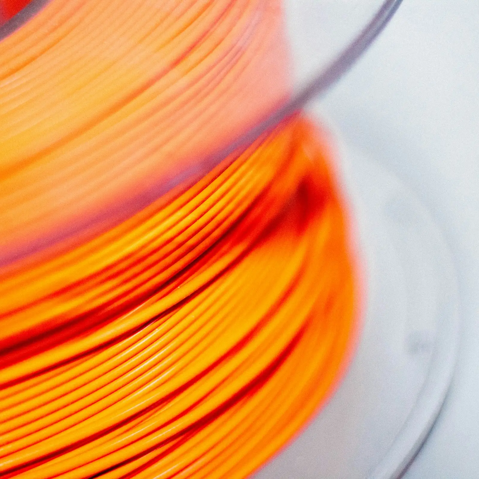 Macro del bobinado de un filamento naranja: las vueltas ordenadas y paralelas sobre el carrete, sin cruces ni huecos