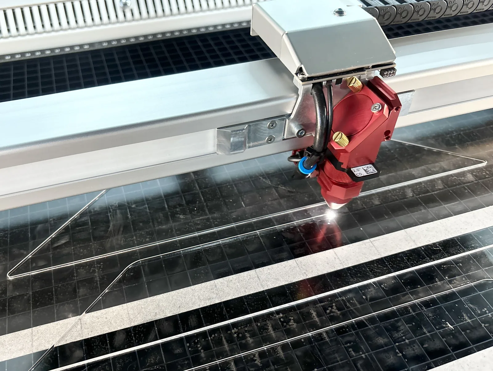 Cabezal de una máquina de CO2 cortando una plancha sobre una mesa de panal, con el punto de incidencia encendido