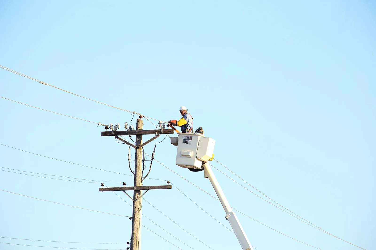Liniero con casco trabajando sobre un poste de distribución eléctrica desde una grúa de canasta