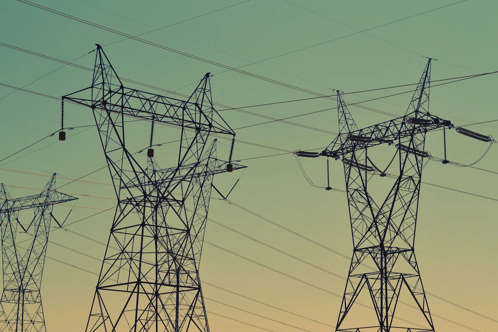 Siluetas de torres de transmisión de alta tensión y sus cables contra un cielo de atardecer