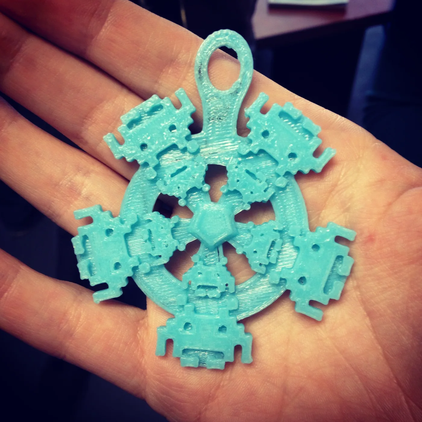 Adorno azul claro impreso en 3D con pequeñas figuras robóticas geométricas, sostenido sobre una mano