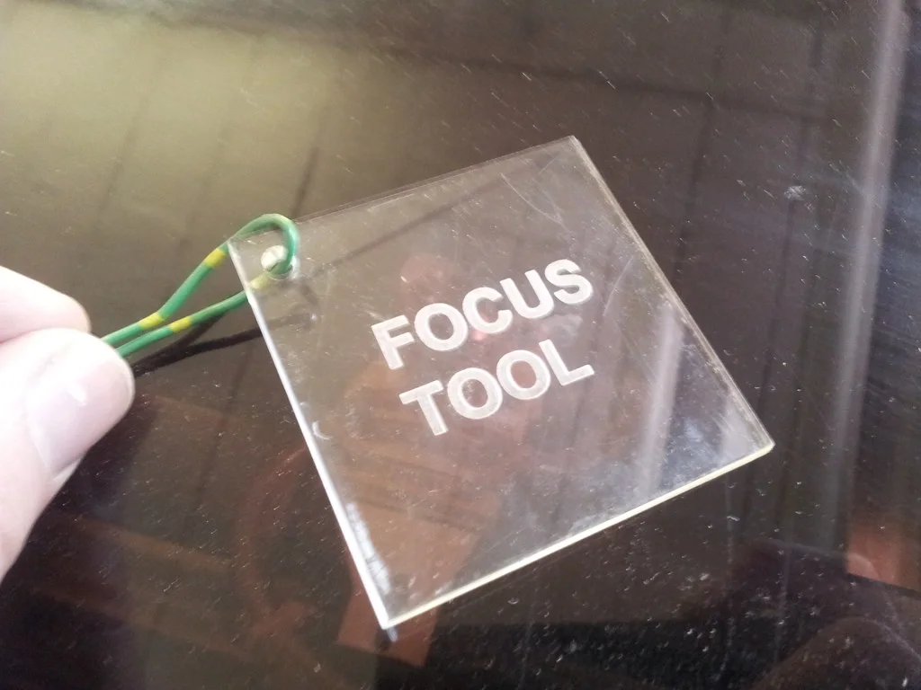 Placa cuadrada de acrílico transparente con las palabras FOCUS TOOL grabadas, colgada de un cordón sobre la máquina