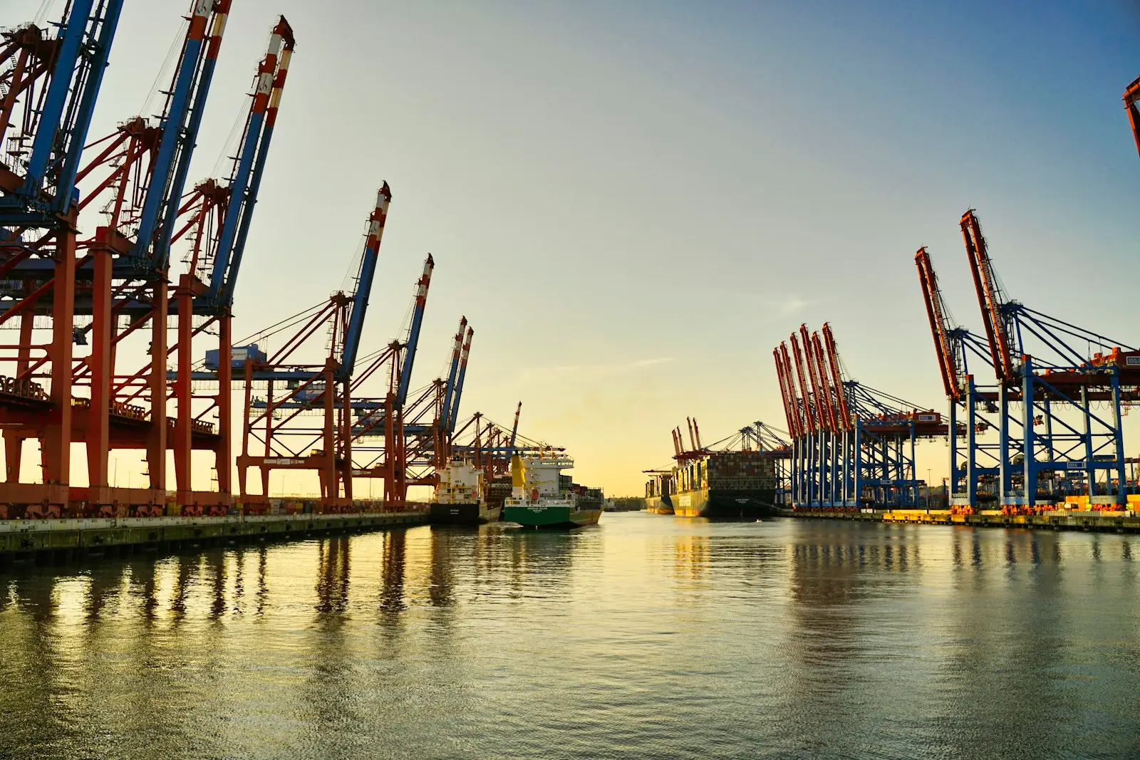Grúas pórtico de una terminal de contenedores portuaria al amanecer, con buques atracados al fondo