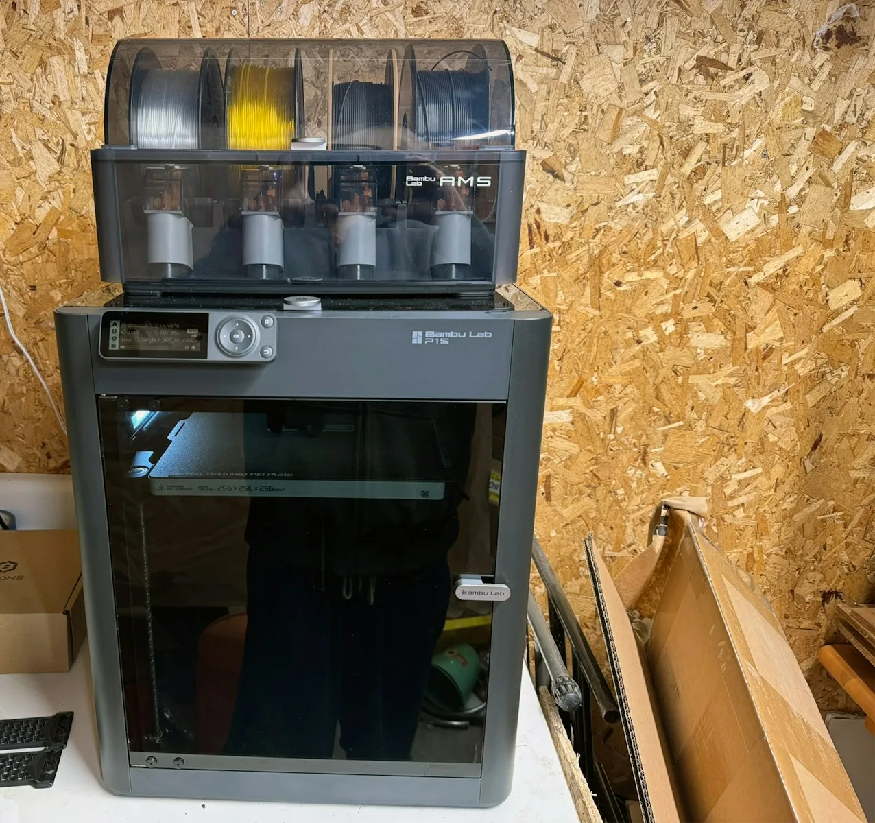 Impresora cerrada Bambu Lab P1S con la unidad AMS de cuatro bobinas montada encima, en un taller casero