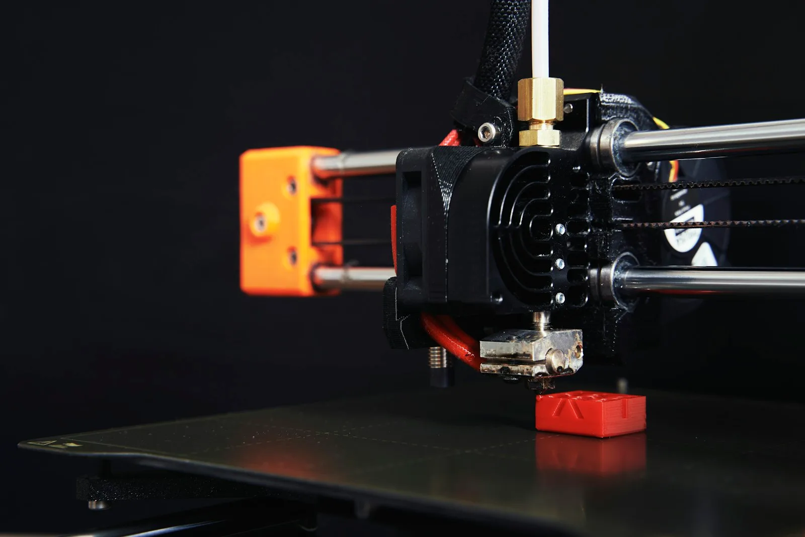 Impresora 3D compacta imprimiendo una pieza roja sobre la cama, fotografiada sobre fondo negro
