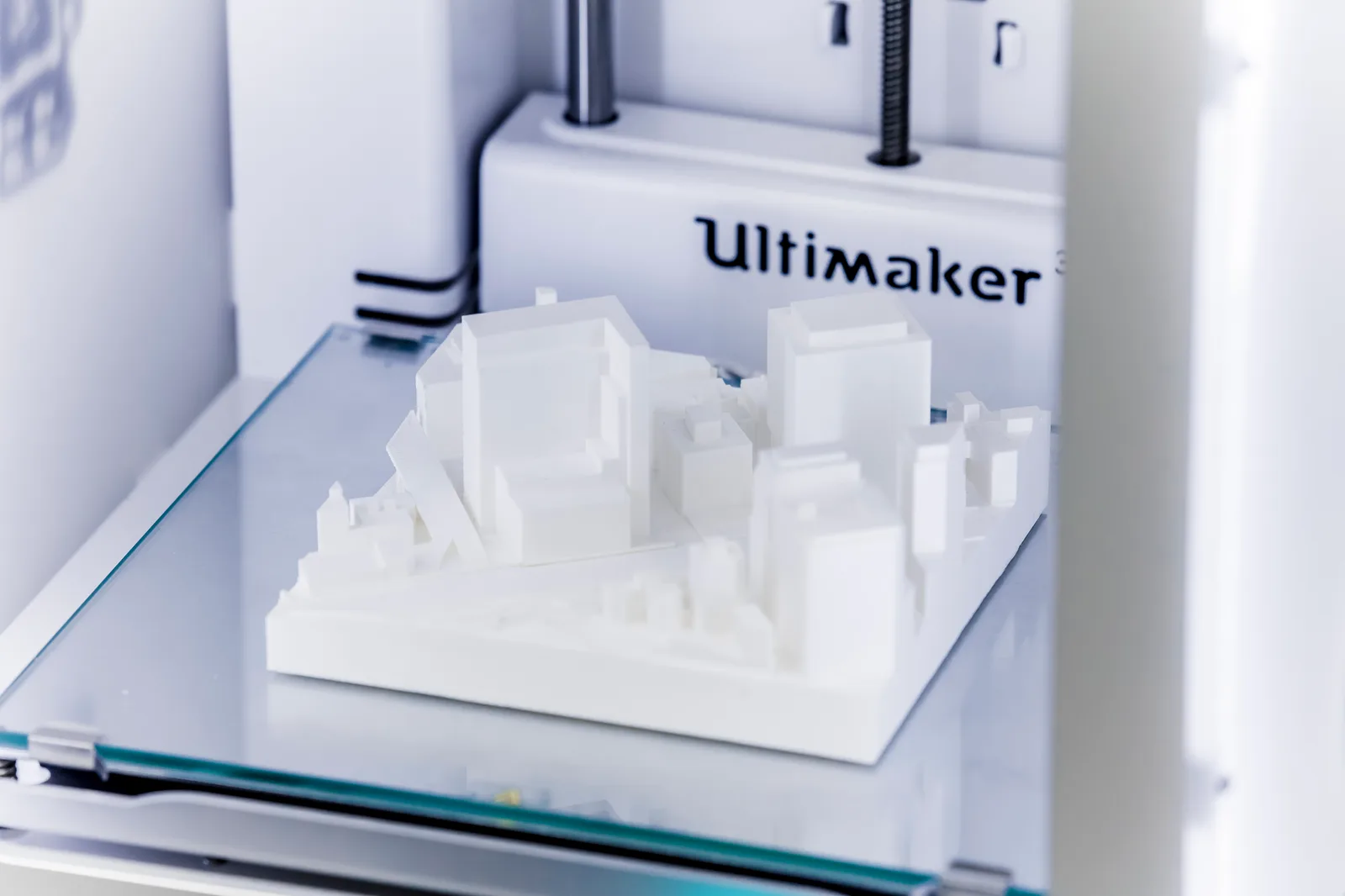 Maqueta urbana blanca recién impresa sobre la cama de cristal de una impresora 3D, con los edificios reducidos a volúmenes