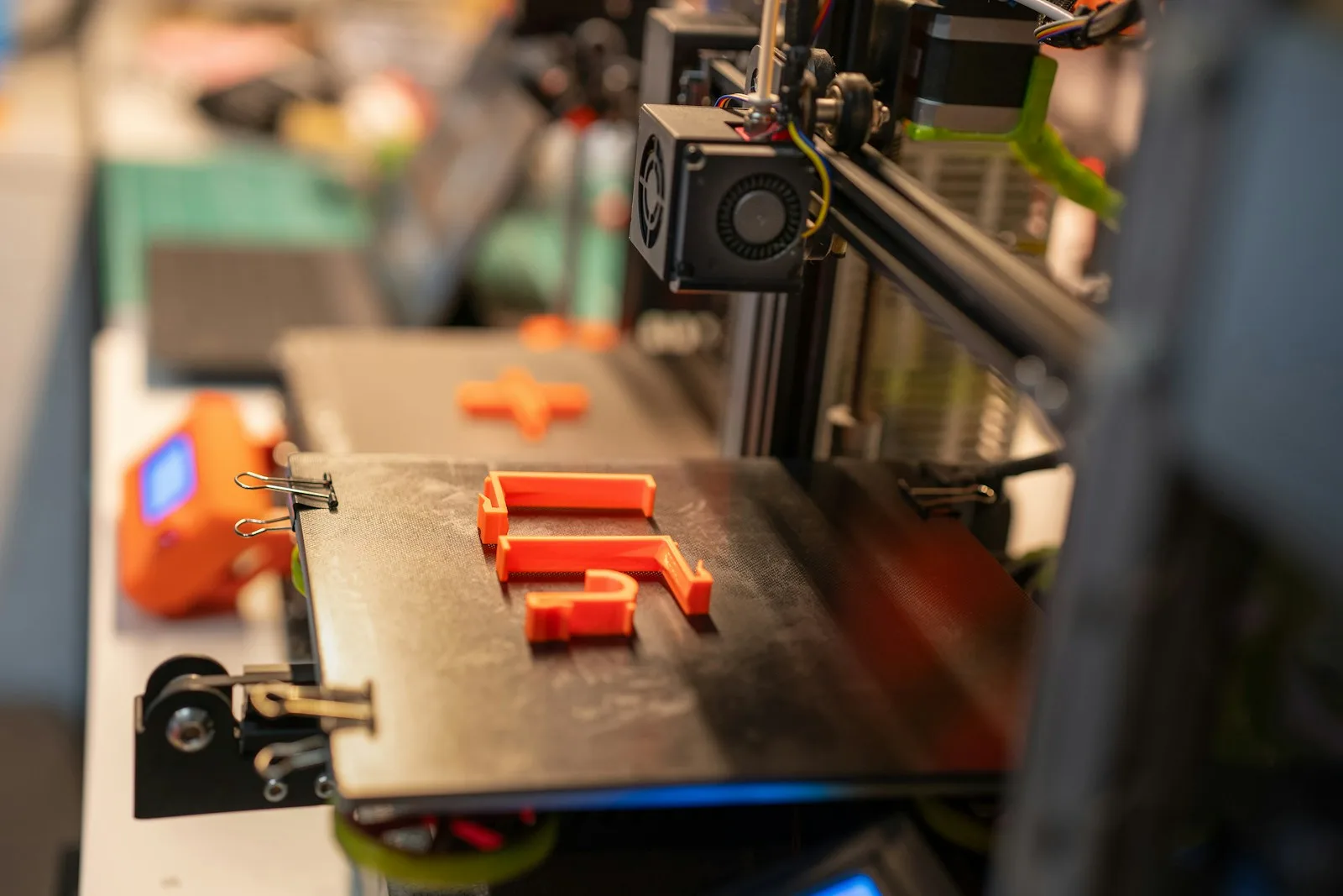 Piezas naranjas recién impresas sobre la cama de una impresora 3D, con las líneas de capa visibles en sus paredes