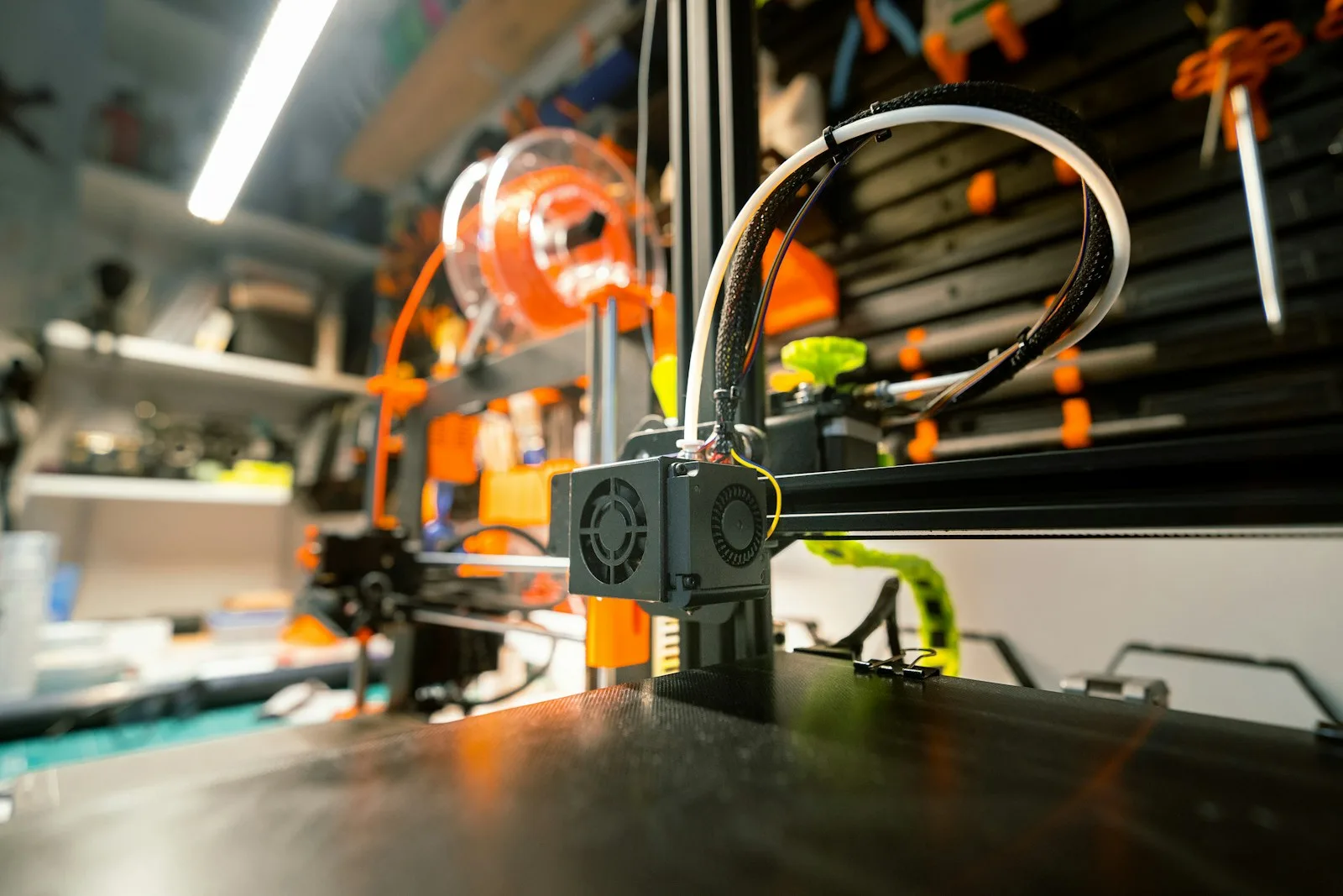 Impresora 3D en un taller casero ordenado, con bobinas de filamento y herramientas en estantes al fondo
