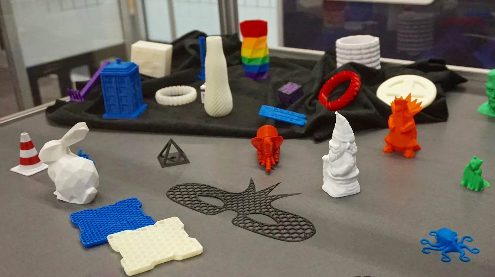 Mesa con una colección de piezas impresas en 3D de distintos colores y formas: figuras pequeñas, cuadrados de prueba y modelos de calibración
