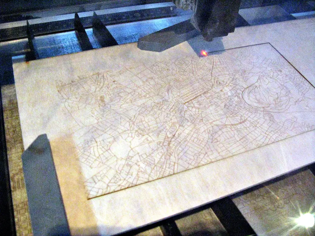 Cabezal de una máquina láser grabando el trazado de un mapa de calles sobre una tabla de madera clara