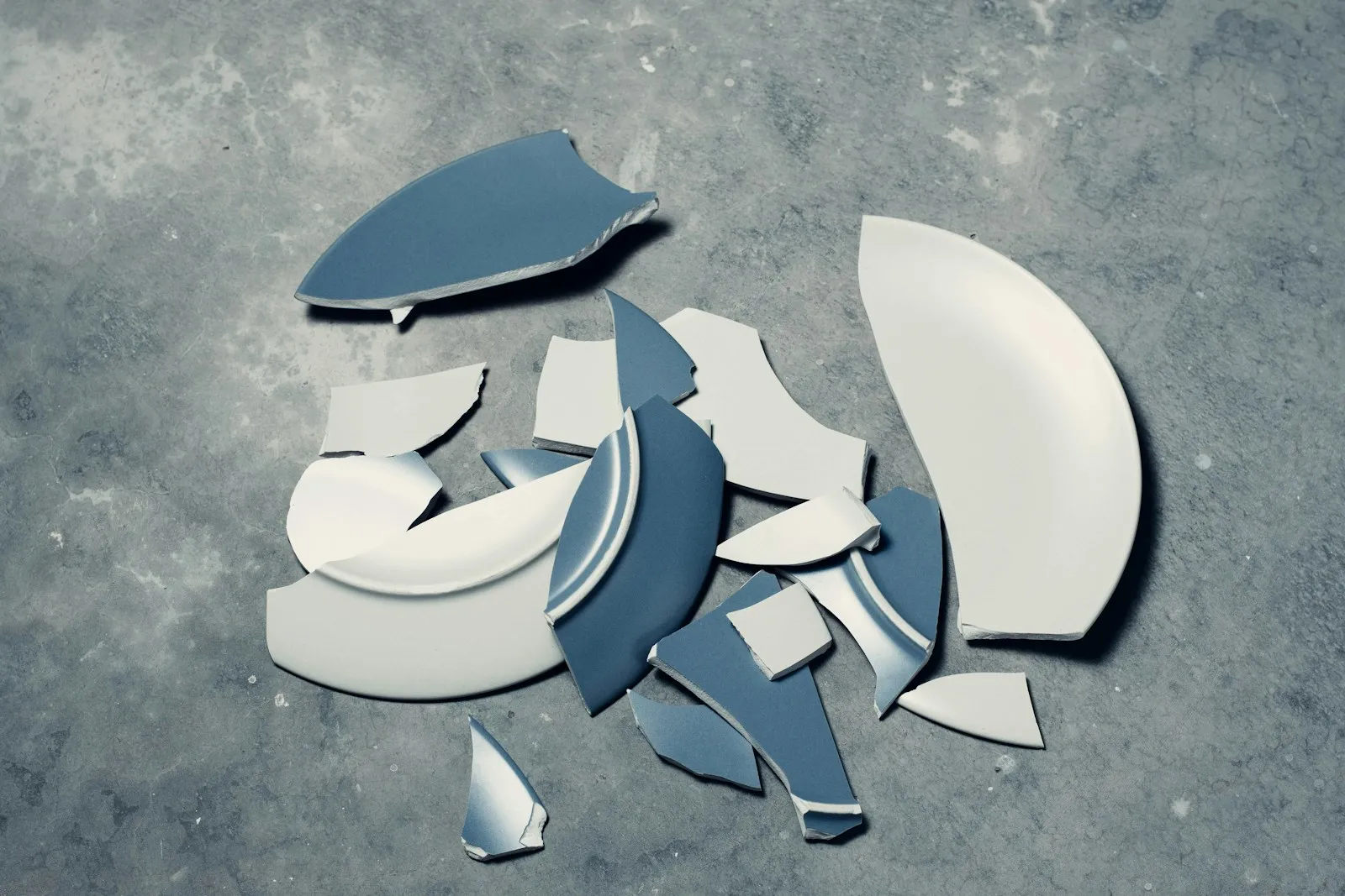 Pieza azul rota en varios fragmentos sobre un suelo de cemento, con los bordes de fractura a la vista