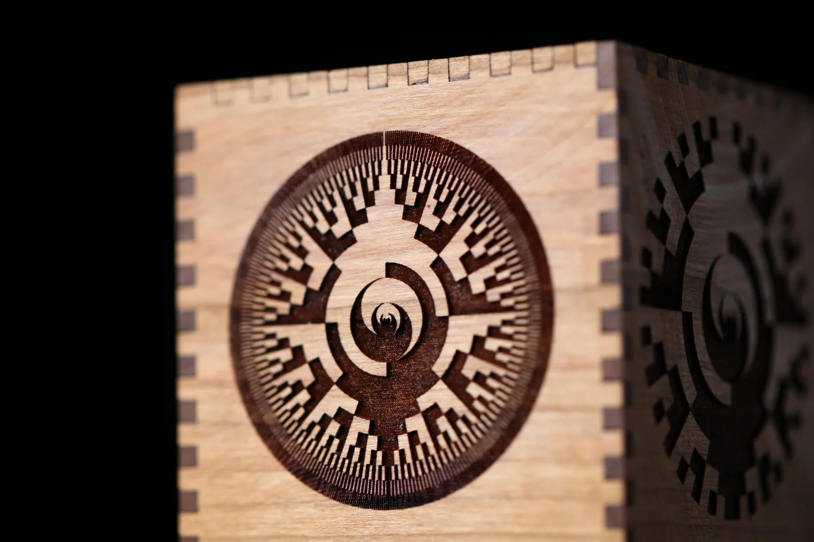 Caja de madera de cerezo con un grabado radial en espiral, oscuro y profundo, sobre la madera clara sin grabar