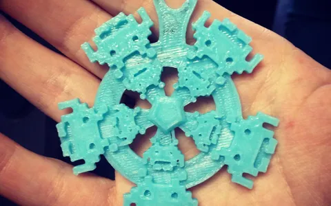 Adorno calado impreso en 3D en filamento turquesa, sostenido en la palma de la mano
